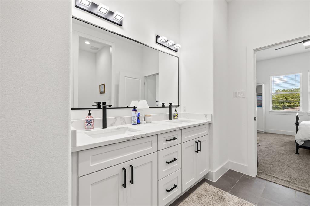 Double vanity featuring white cabinetry, stone-finish countertops with integrated sinks, matte black hardware, and dual wall-mounted light fixtures