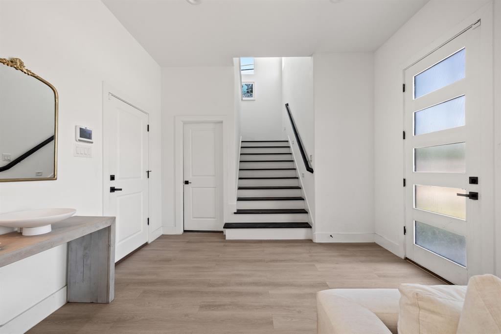 Entryway featuring wood-finish flooring, a contemporary door with horizontal glass panels, a floating vanity with a vessel sink, and a staircase with contrasting dark treads Entryway featuring wood-finish flooring, a contemporary door with horizontal glass panels, a floating vanity with a vessel sink, and a staircase with contrasting dark treads