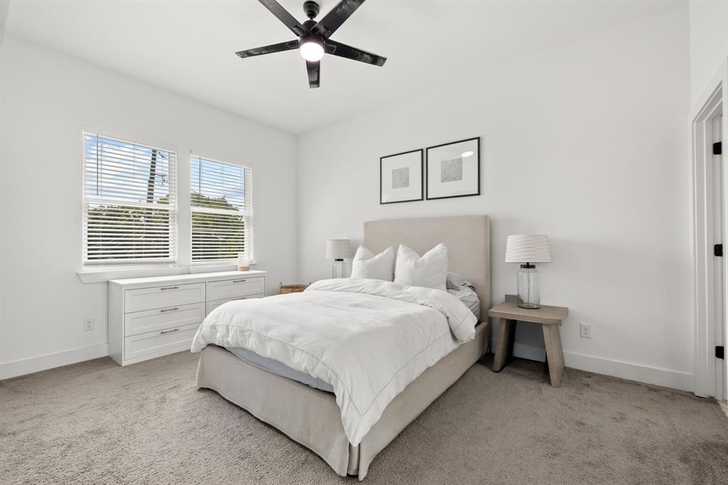 Neutral interior featuring plush wall-to-wall carpeting, high ceilings, large dual-pane windows with horizontal blinds, and a modern matte black ceiling fan with integrated lighting
