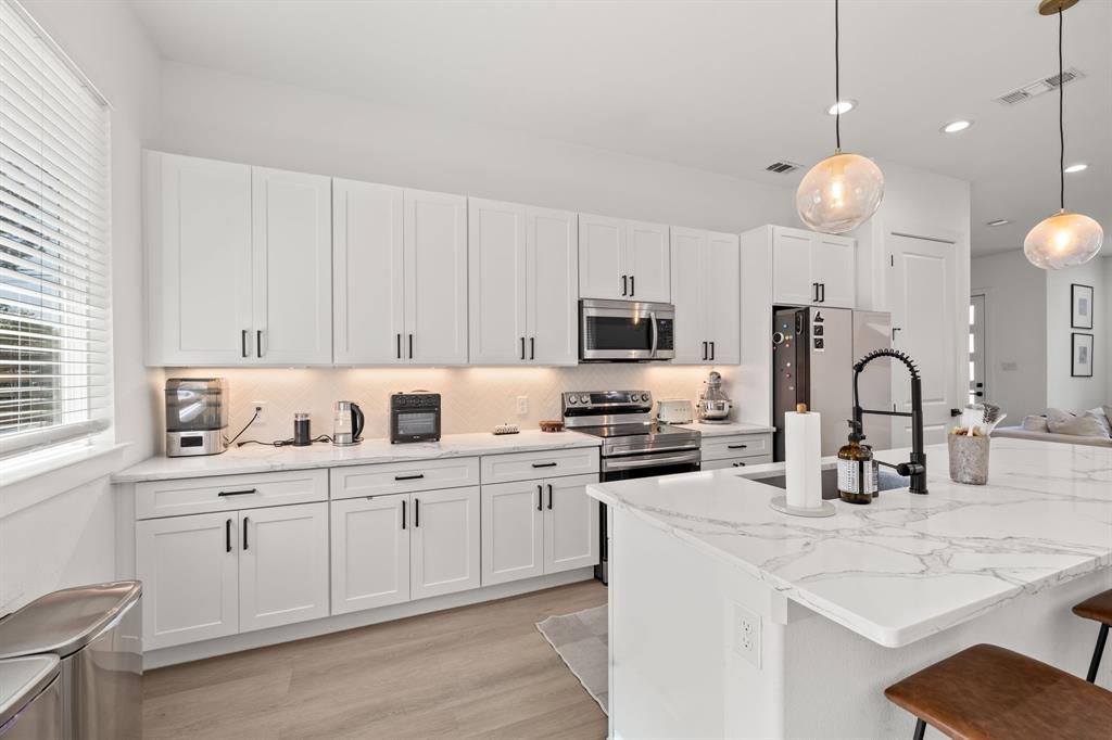 Kitchen featuring white shaker-style cabinetry, white countertops with grey veining, a central island with a matte black faucet, stainless steel appliances, and wood-finish flooring Kitchen featuring white shaker-style cabinetry, white countertops with grey veining, a central island with a matte black faucet, stainless steel appliances, and wood-finish flooring