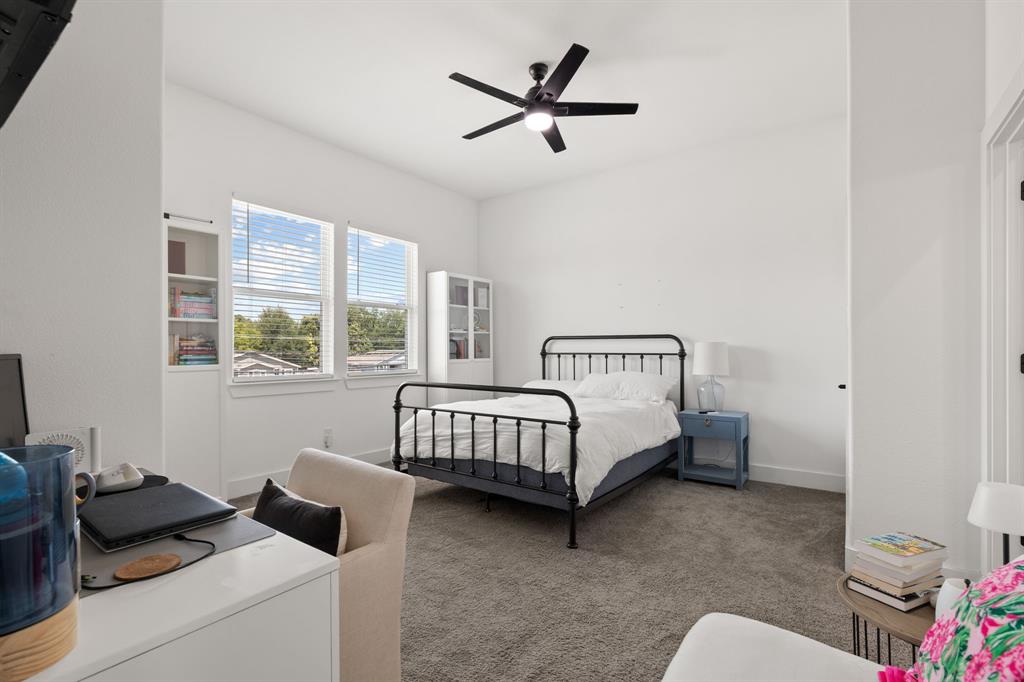 High-ceiling room featuring neutral carpeting, a ceiling fan with integrated lighting, dual windows, and built-in shelving