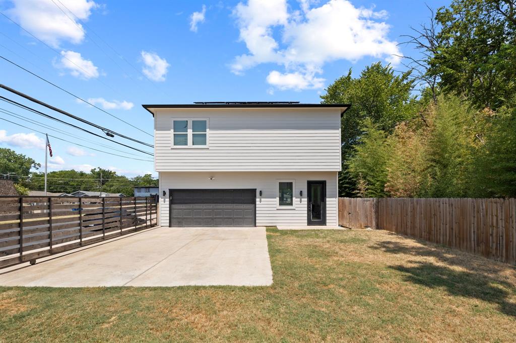 Two-story exterior featuring horizontal siding, a private concrete parking pad, a two-car garage with a paneled door, and wood-style fencing