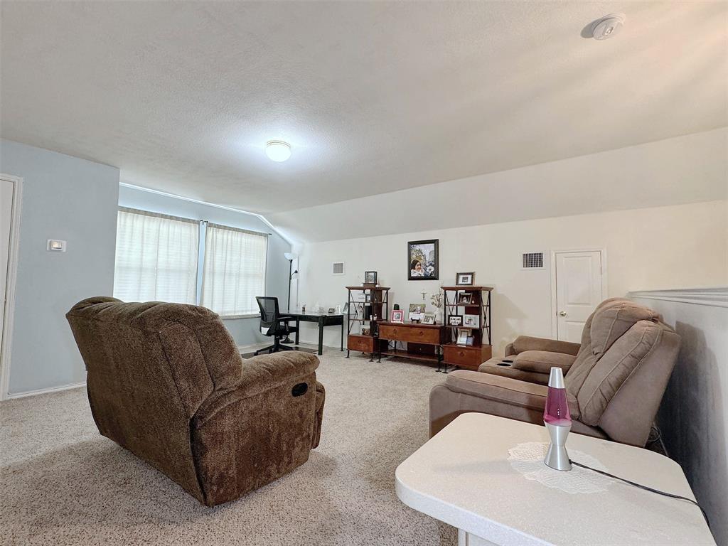 Wide view of the furnished living room, showing its seating area, light-colored walls, ceiling detail, and connection to the adjoining interior spaces.