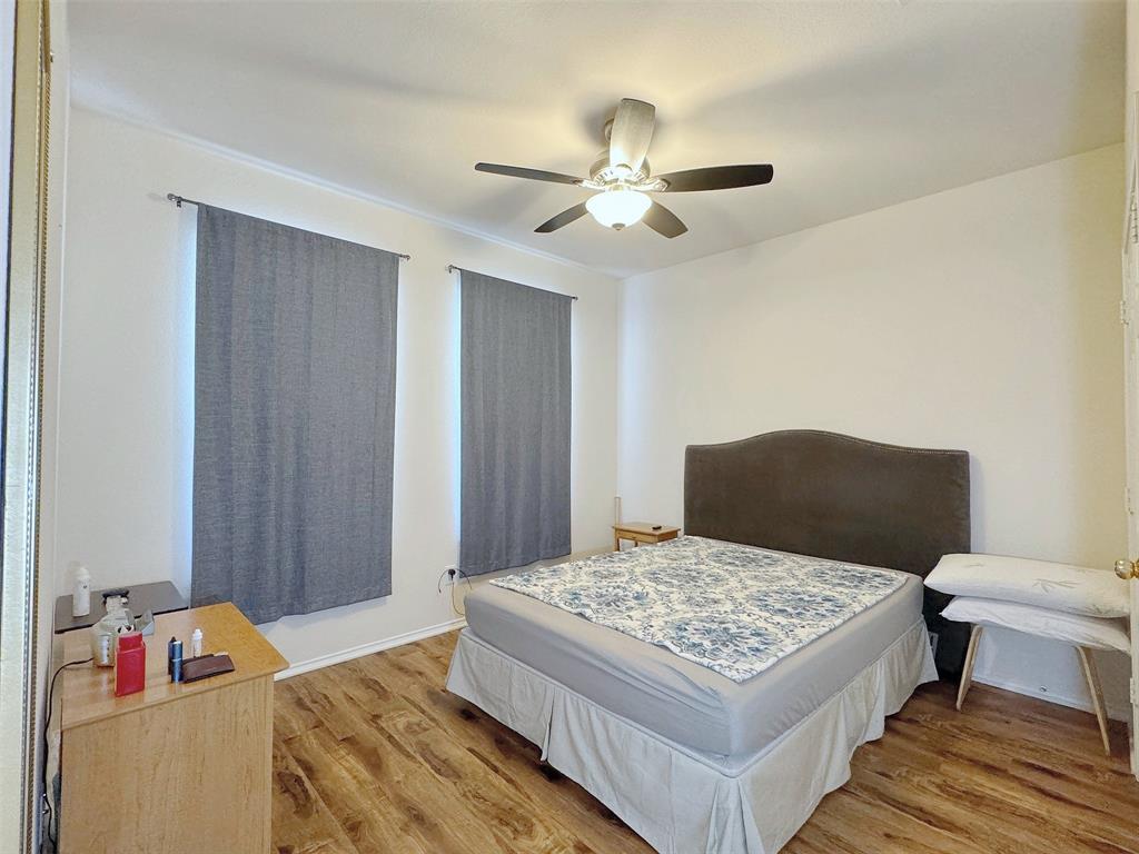 Bedroom with wood-look flooring, a ceiling fan with light, window coverings, and furnishings that illustrate the room layout.