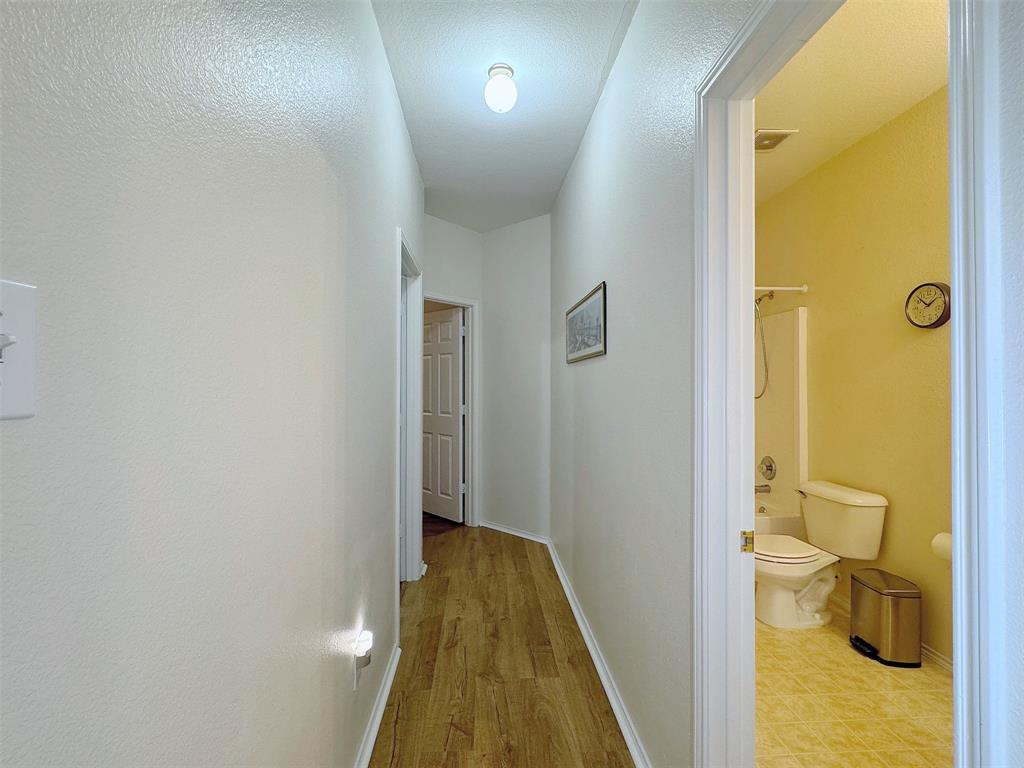 Interior hallway with wood-look flooring, ceiling lighting, and doorways connecting the adjoining rooms; a bathroom is visible at the side.