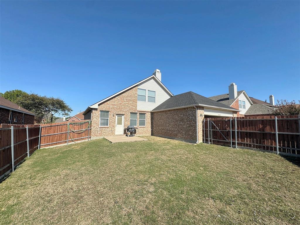 Alternate backyard view showing the rear elevation, lawn, concrete patio, and fenced outdoor space.