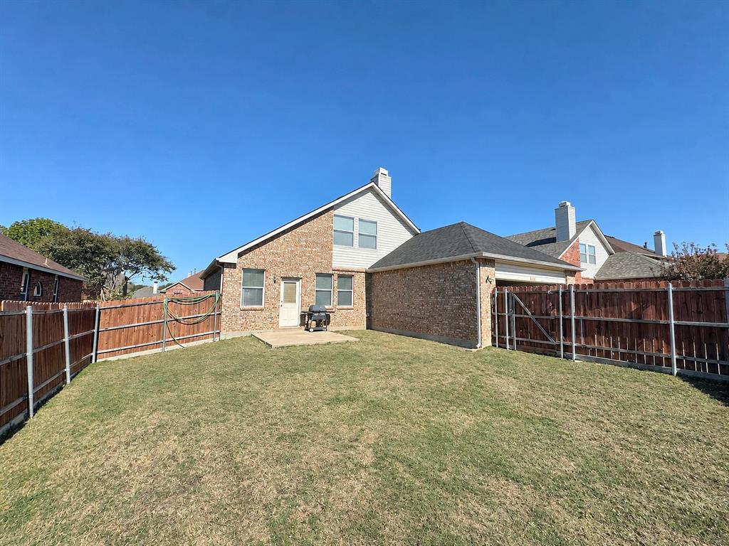 Ground-level backyard view showing the rear brick-and-siding exterior, lawn, patio area, and wood perimeter fencing.