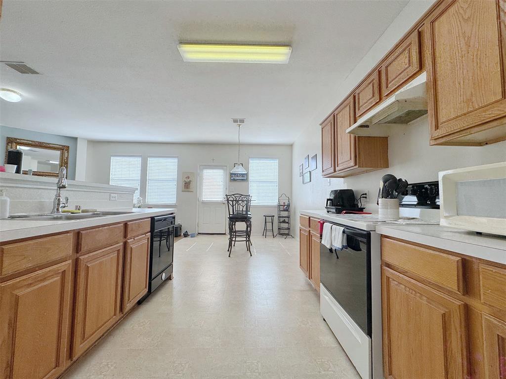 Kitchen view highlighting wood cabinetry, light countertops, cooking appliances, and a central walkway toward the windowed dining area.