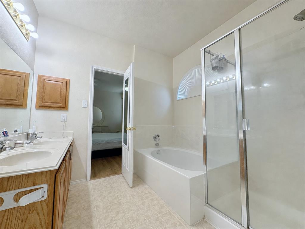 Bathroom view showing the glass-enclosed shower, adjacent bathtub, light-colored tile, and part of the vanity area.