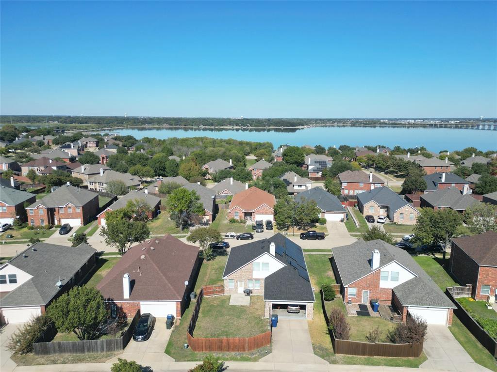 Wide aerial view showing the home within the surrounding neighborhood, including nearby streets, rooftops, and water visible in the distance.