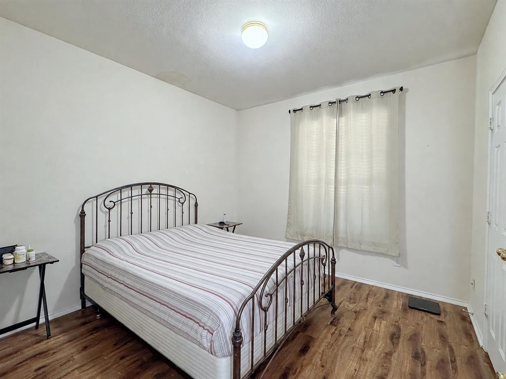 Bedroom with a metal bed frame, wood-look flooring, light-colored walls, and a curtained window.