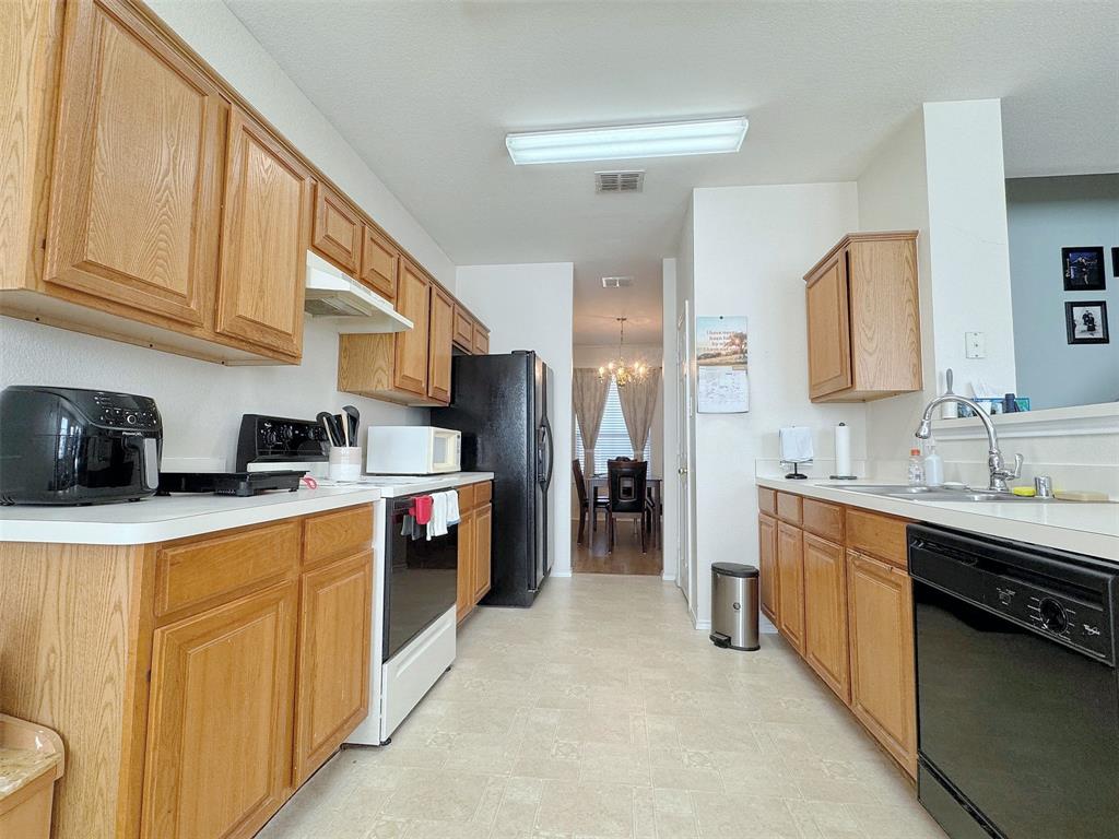 Reverse kitchen angle showing cabinetry on both sides, counter workspace, the sink area, appliances, and the passage through the kitchen.