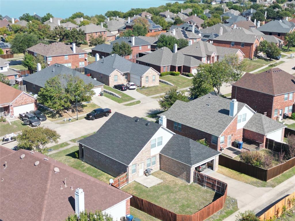 Oblique aerial view showing the rear of the home, roofline, fenced yard, driveway, and surrounding residential lots.