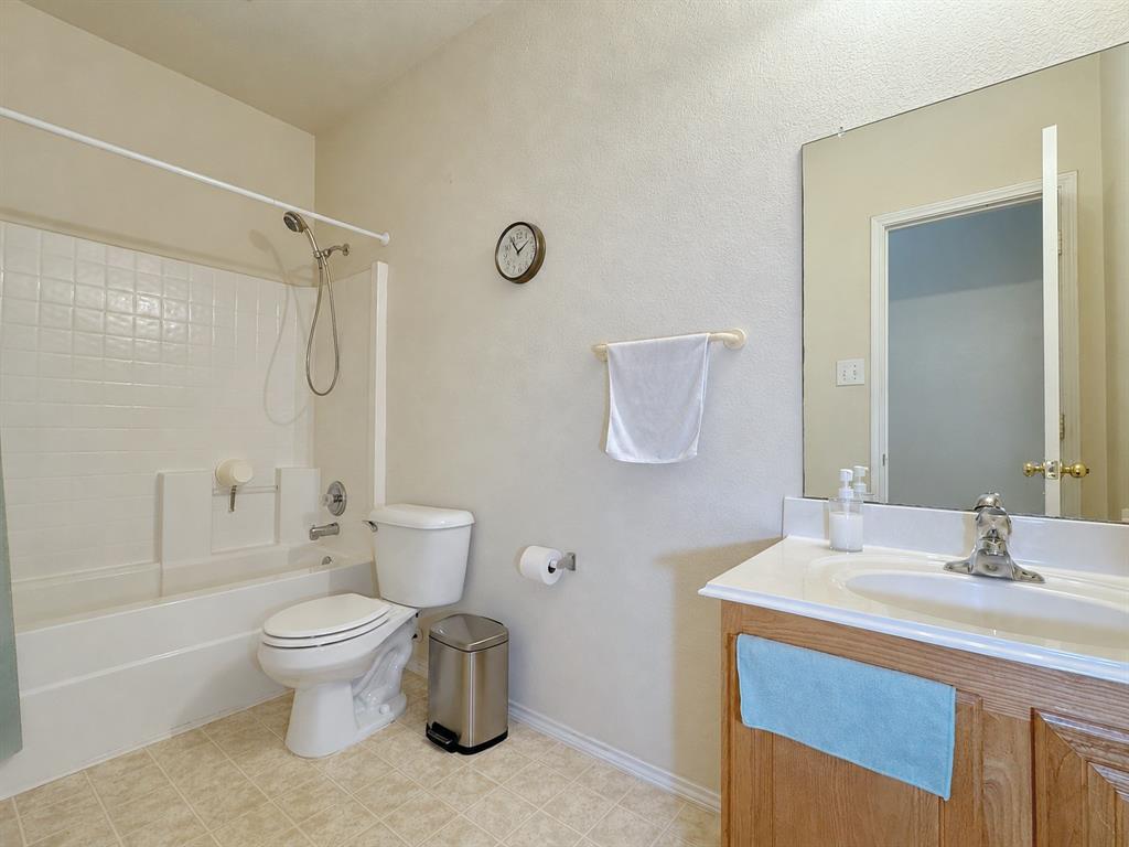 Bathroom with a tub-and-shower combination, toilet, wood vanity, light countertop, and wall mirror.