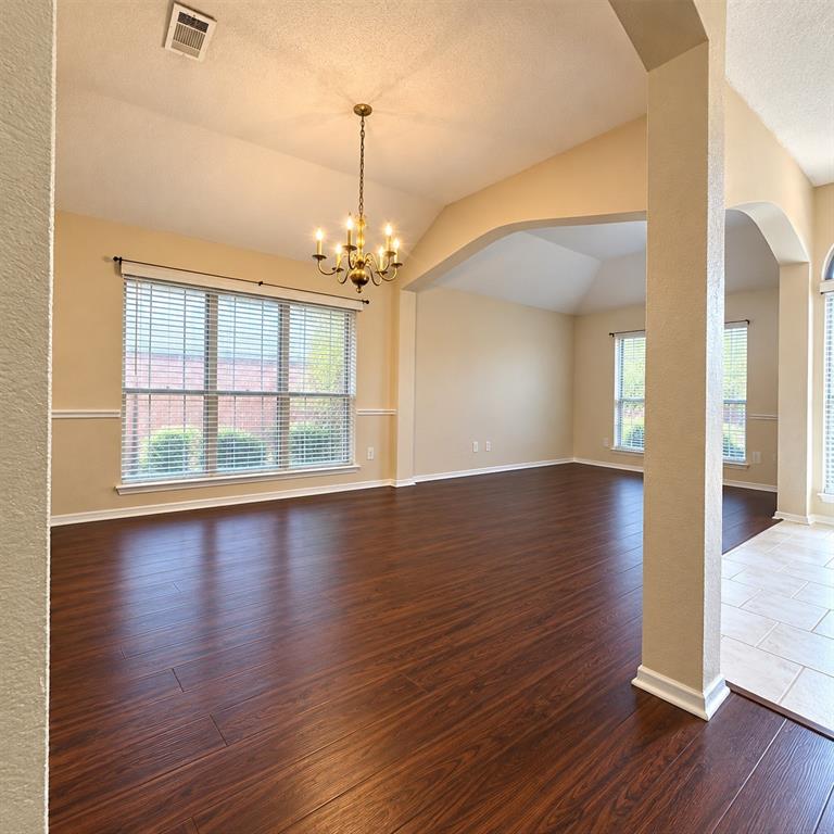 Vaulted ceilings featuring decorative arched architectural detailing, wood-finish flooring, multi-pane windows, and a traditional six-arm chandelier