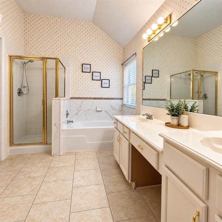 Bathroom featuring a dual-sink vanity with a solid-surface countertop, a separate shower enclosure with gold-tone hardware, a deep soaking tub with decorative tile surround, and a wall-to-wall vanity mirror