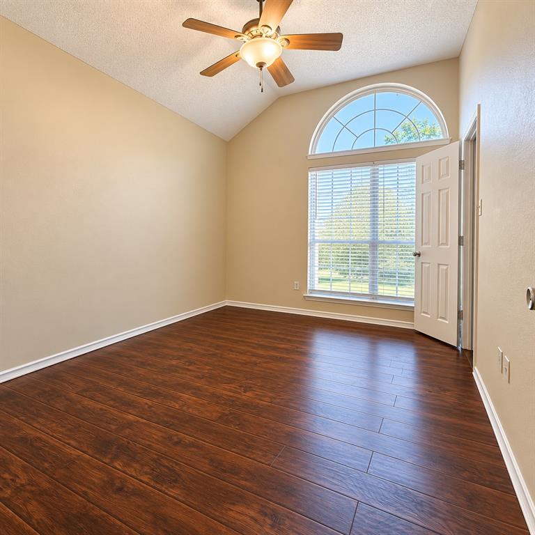 Vaulted ceiling, wood-finish flooring, arched transom window, and ceiling fan with integrated light fixture