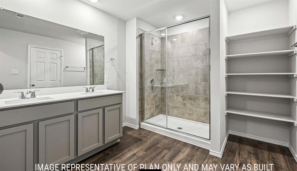 Dual-sink vanity with light-colored countertops, oversized wall-to-wall mirror, enclosed walk-in shower with tile surround, and built-in shelving finished with wood-finish flooring