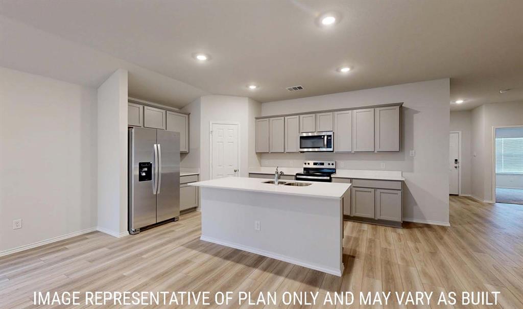 Kitchen featuring a central island with a solid surface countertop, light-toned cabinetry, stainless steel appliances, recessed ceiling lighting, and wood-finish flooring Kitchen featuring a central island with a solid surface countertop, light-toned cabinetry, stainless steel appliances, recessed ceiling lighting, and wood-finish flooring