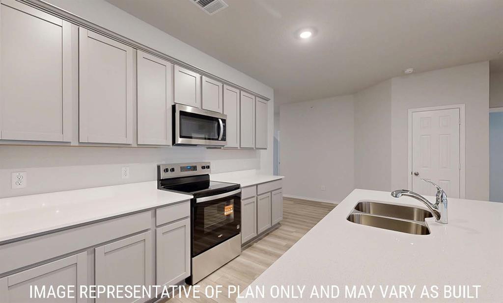 Kitchen featuring shaker-style cabinetry, solid-surface countertops, stainless steel appliances, a central island with an integrated dual-basin sink, and wood-finish flooring Kitchen featuring shaker-style cabinetry, solid-surface countertops, stainless steel appliances, a central island with an integrated dual-basin sink, and wood-finish flooring
