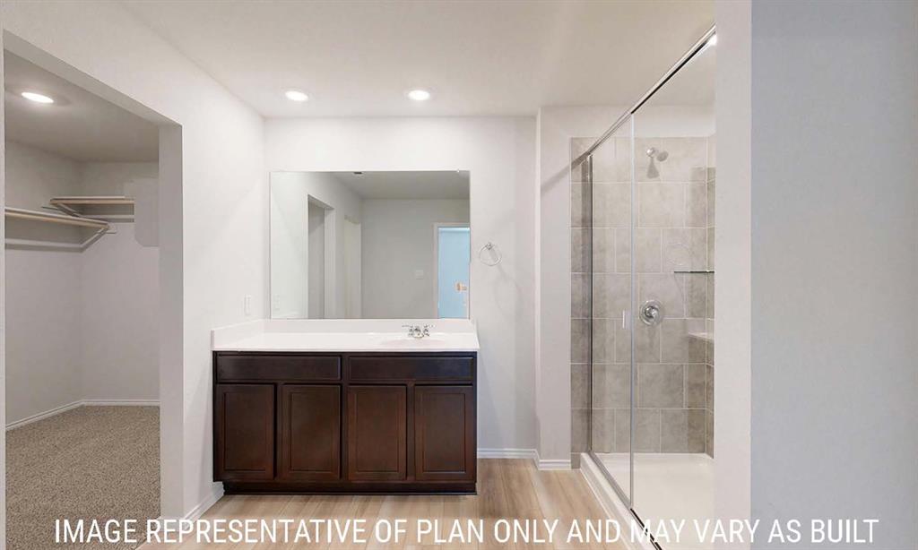 Bathroom featuring a dark wood-finish vanity, solid-surface countertop, full-width mirror, walk-in shower with glass enclosure, and built-in closet shelving