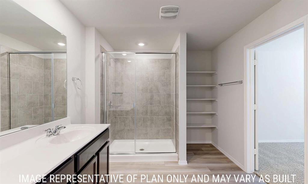 Bathroom featuring a walk-in shower with tile surround, glass enclosure, vanity with integrated sink, and built-in shelving