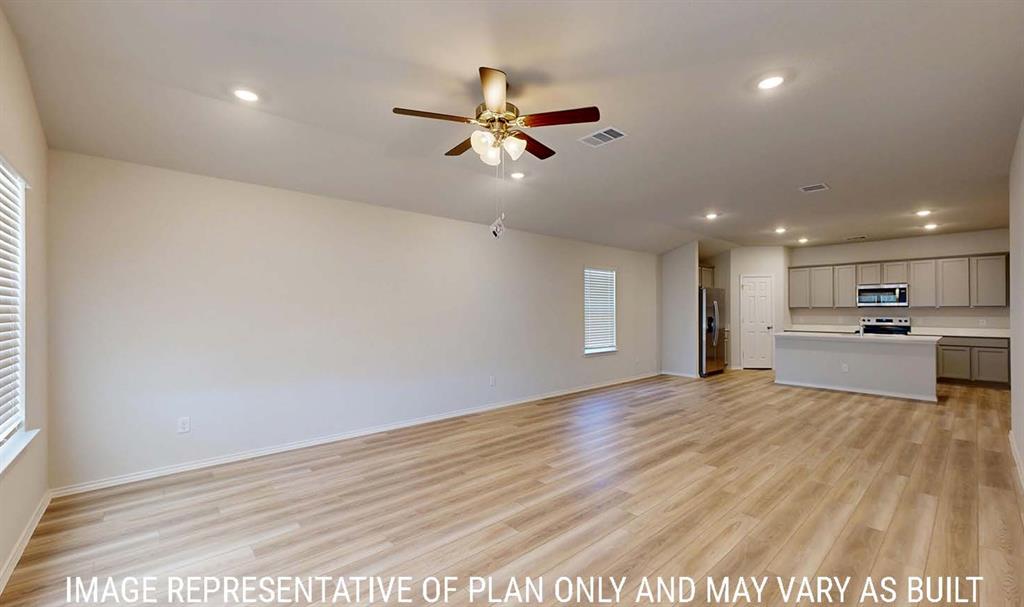 Open-concept interior featuring light wood-finish flooring, recessed lighting, a ceiling fan with integrated lighting, and a kitchen equipped with cabinetry and a breakfast bar