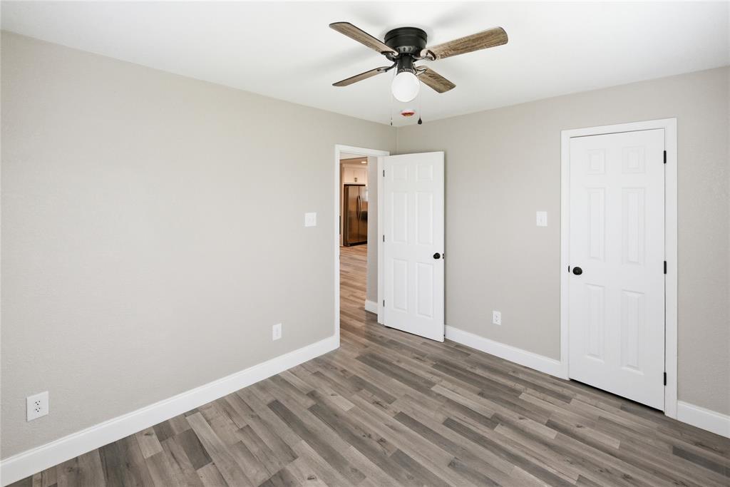 Room featuring wood-finish flooring, a ceiling fan with integrated lighting, neutral wall paint, and two six-panel interior doors Room featuring wood-finish flooring, a ceiling fan with integrated lighting, neutral wall paint, and two six-panel interior doors