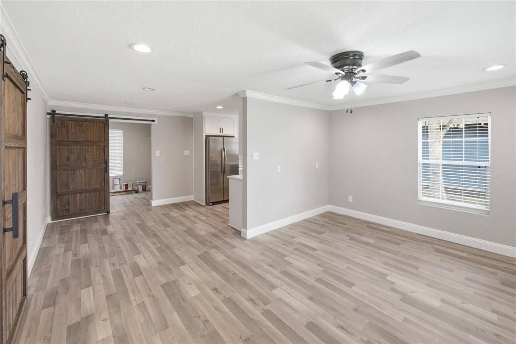 Wood-finish flooring, sliding barn door with dark hardware, recessed lighting, ceiling fan with light kit, and stainless steel refrigerator Wood-finish flooring, sliding barn door with dark hardware, recessed lighting, ceiling fan with light kit, and stainless steel refrigerator