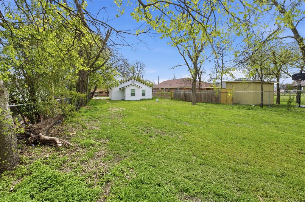 Expansive backyard featuring a large grass lawn, mature trees, wood privacy fencing, and a detached storage structure