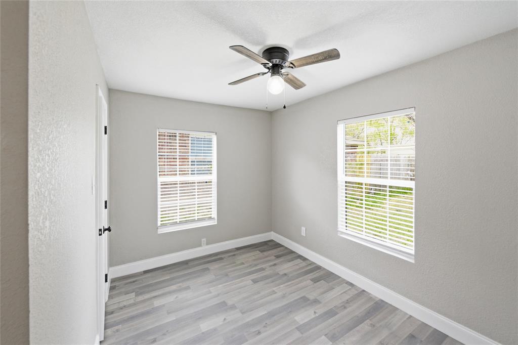 Neutral-toned interior featuring wood-finish flooring, dual windows with fitted blinds, and a central ceiling fan