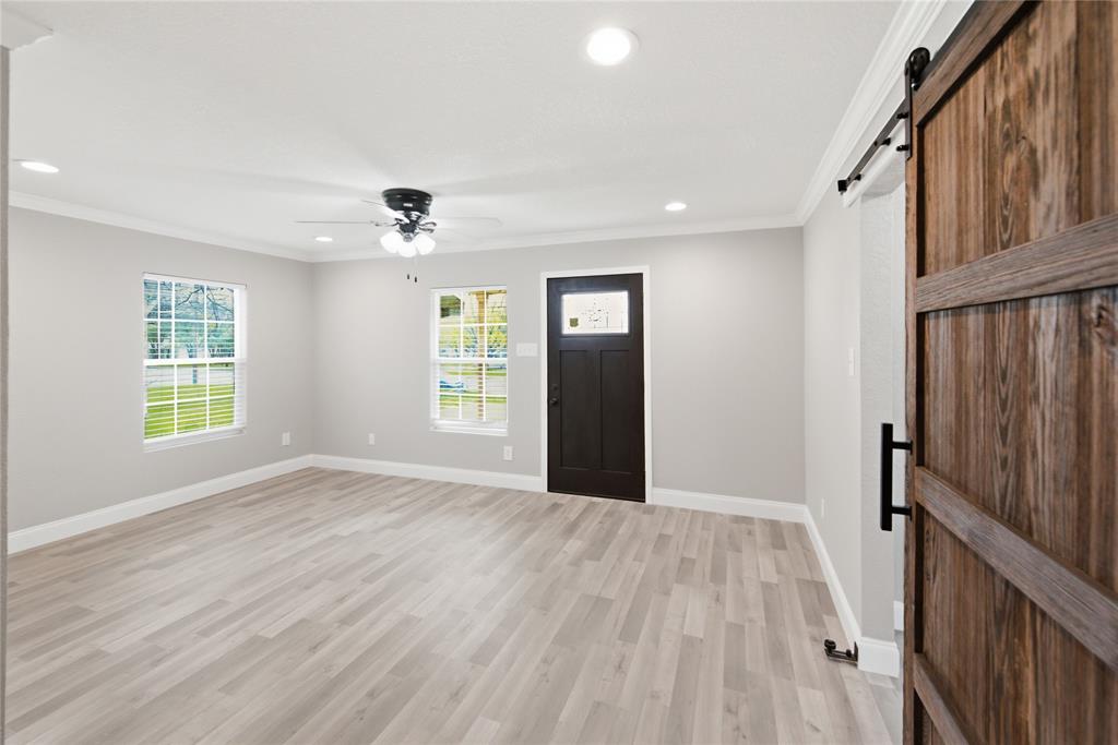Interior space featuring wood-finish flooring, recessed lighting, a ceiling fan with integrated light fixture, windows with white trim, and a wooden sliding barn door with black hardware Interior space featuring wood-finish flooring, recessed lighting, a ceiling fan with integrated light fixture, windows with white trim, and a wooden sliding barn door with black hardware