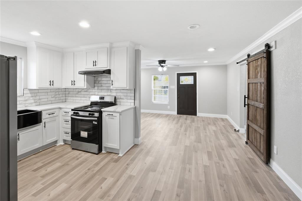 Kitchen featuring white shaker-style cabinetry, a light-toned tile backsplash, wood-finish flooring, and a sliding barn-style door Kitchen featuring white shaker-style cabinetry, a light-toned tile backsplash, wood-finish flooring, and a sliding barn-style door