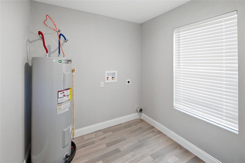 Utility room featuring wood-finish flooring, a vertical water heater, wall-mounted water hookups, and a window with horizontal blinds