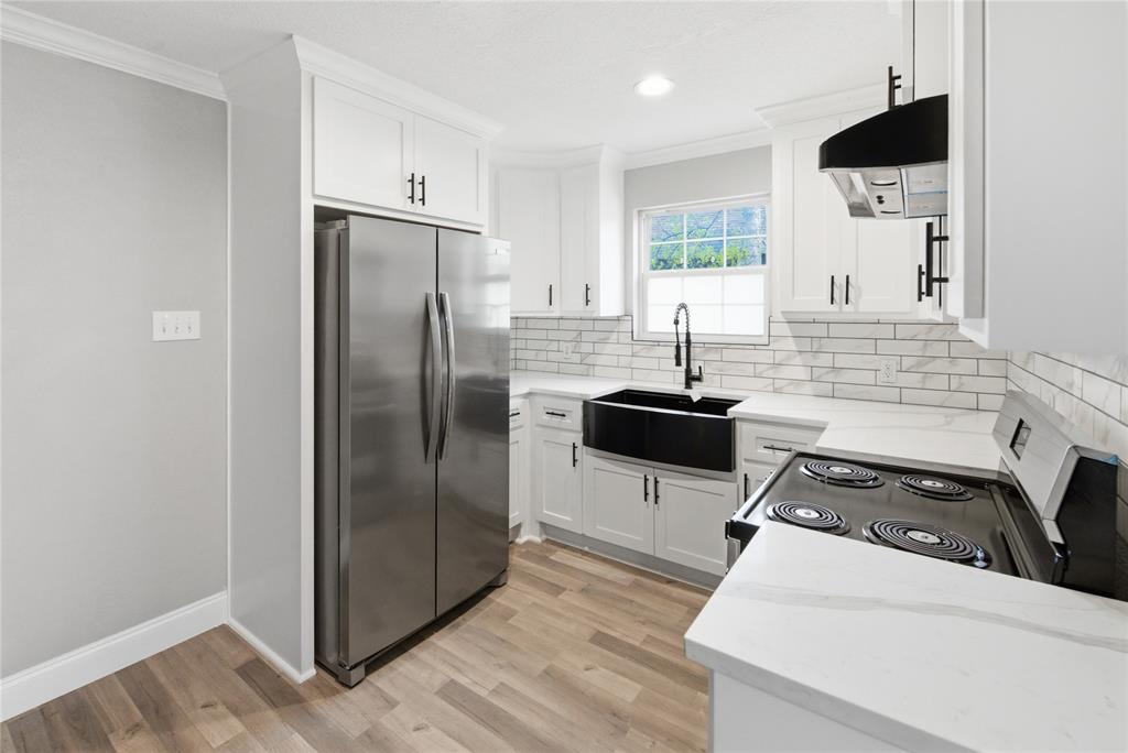 Kitchen featuring white cabinetry with matte black hardware, stone-finish countertops, subway tile backsplash, farmhouse-style sink with a pull-down faucet, and wood-finish flooring Kitchen featuring white cabinetry with matte black hardware, stone-finish countertops, subway tile backsplash, farmhouse-style sink with a pull-down faucet, and wood-finish flooring