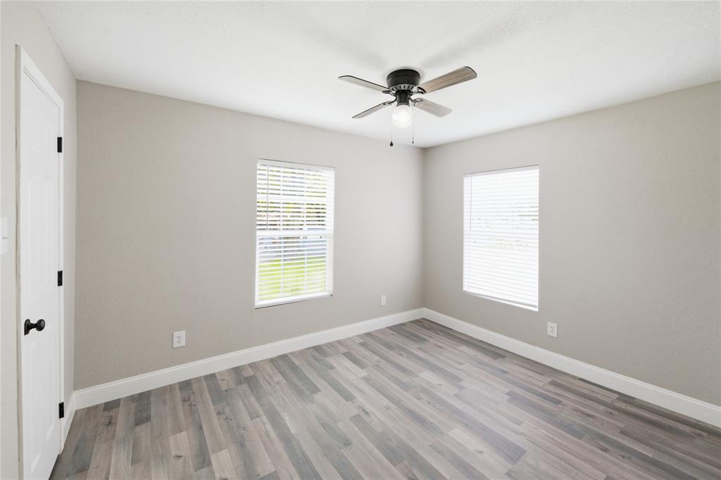 Room featuring wood-finish flooring, two windows with horizontal blinds, neutral wall paint, and a ceiling fan with integrated light fixture Room featuring wood-finish flooring, two windows with horizontal blinds, neutral wall paint, and a ceiling fan with integrated light fixture