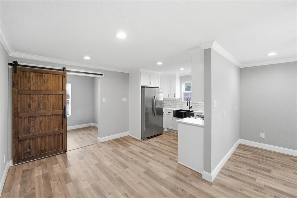 Kitchen featuring white cabinetry, wood-finish flooring, a sliding barn-style door, stainless steel refrigerator, and a farmhouse-style sink with matte black hardware