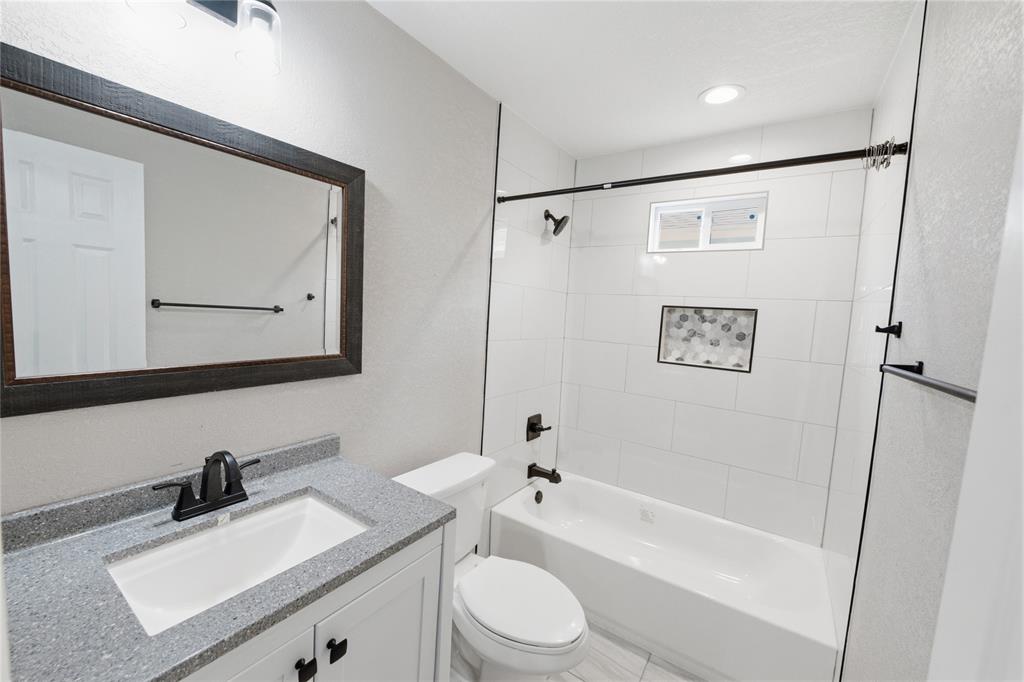 Bathroom featuring a vanity with stone-finish countertop, undermount sink, matte black hardware, tiled shower surround with an inlaid mosaic niche, and a framed mirror