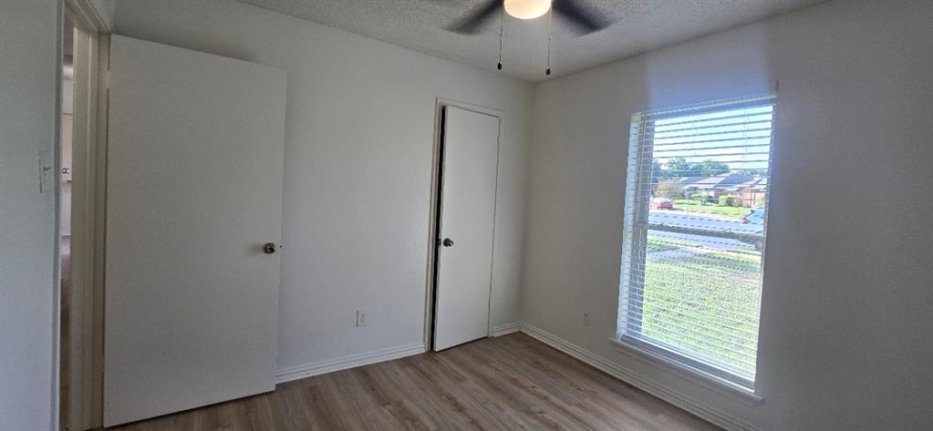 Interior room featuring wood-finish flooring, a ceiling fan with integrated lighting, and a window with horizontal blinds