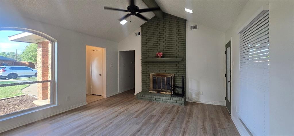 Vaulted ceilings, wood-finish flooring, brick-faced fireplace with a mantel, skylights, and ceiling fan