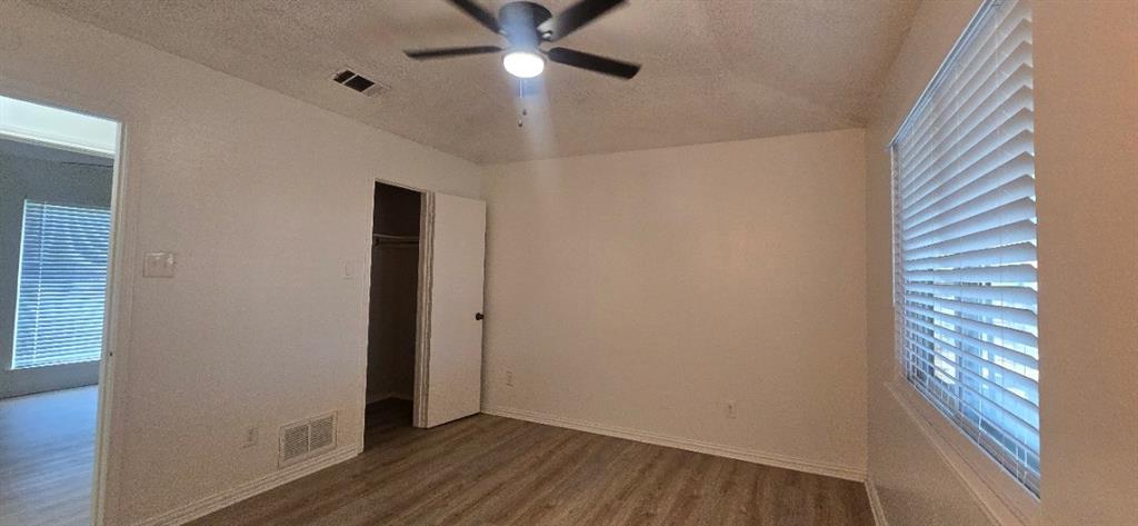 Neutral interior room featuring wood-finish flooring, a ceiling fan with integrated lighting, and horizontal window blinds