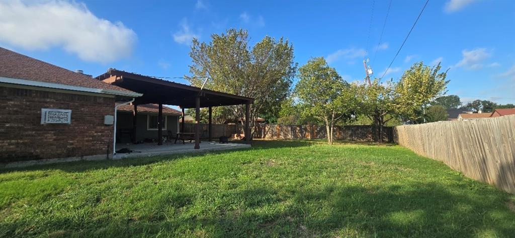 Backyard featuring a covered patio, brick exterior, wood-style privacy fencing, and mature trees