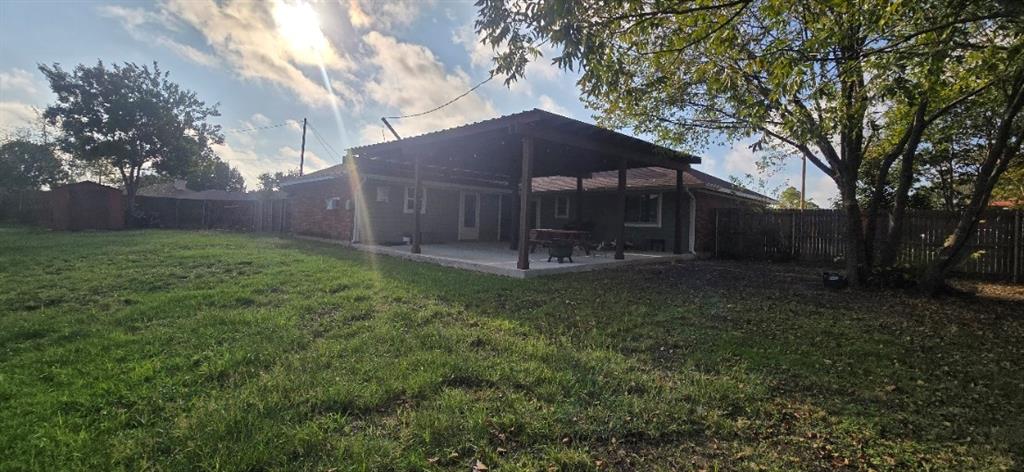 Spacious backyard featuring a large covered patio with a wood-frame structure and wood fencing