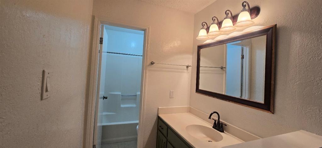 Bathroom featuring a vanity with an integrated basin, multi-bulb light fixture, framed wall mirror, and a tub-shower combination with a surround
