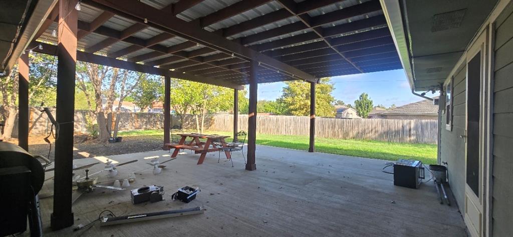 Covered patio featuring an exposed beam ceiling, concrete flooring, support columns, and a fenced backyard