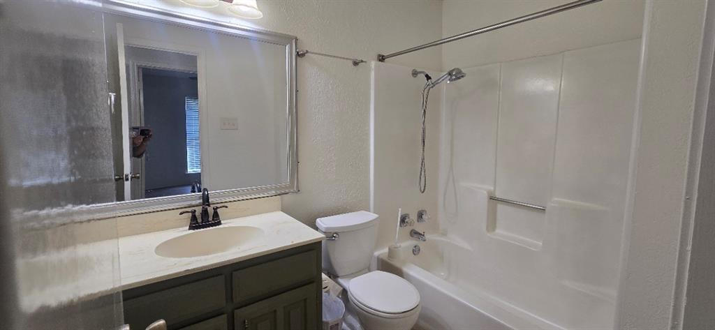 Bathroom featuring a vanity with an integrated basin, a large framed wall mirror, a commode, and a tub-shower combination with a showerhead fixture