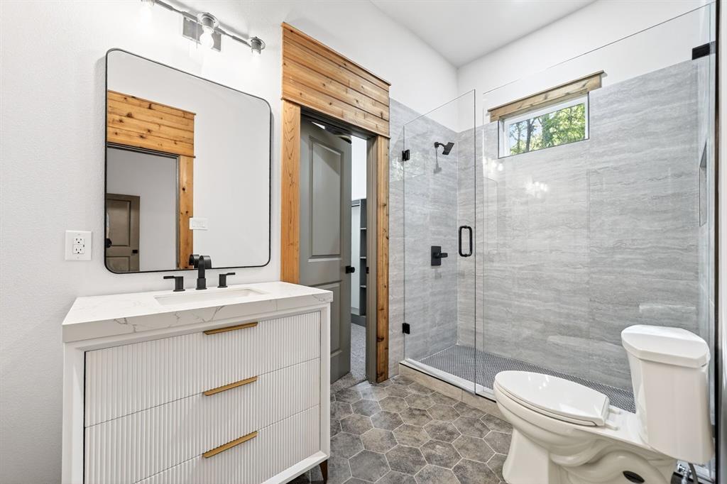 Bathroom featuring a fluted vanity with a stone countertop, walk-in shower with floor-to-ceiling tile, frameless glass enclosure, matte black fixtures, and hexagonal floor tile