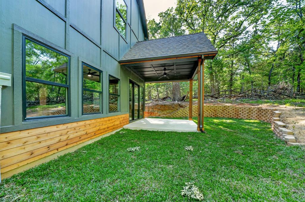 Exterior featuring board and batten siding with natural wood-plank accents, a covered patio with a ceiling fan, a concrete slab, and a multi-tiered stone retaining wall
