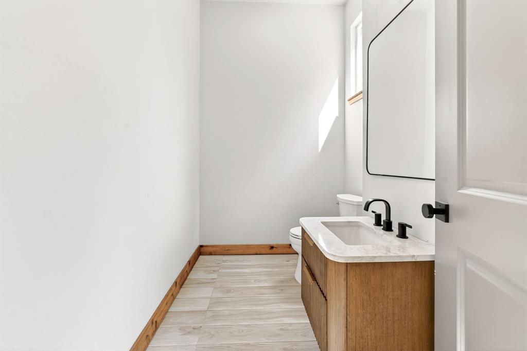 Bathroom vanity featuring a natural wood-finish cabinet, stone-top surface with an integrated sink, matte black widespread faucet, and a coordinating framed rectangular mirror
