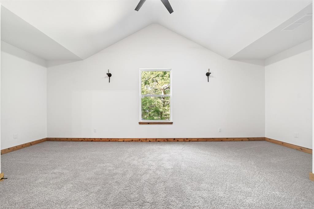 Vaulted ceiling featuring a central ceiling fan, neutral wall-to-wall carpeting, wood trim detailing, and dual wall-mounted light fixtures
